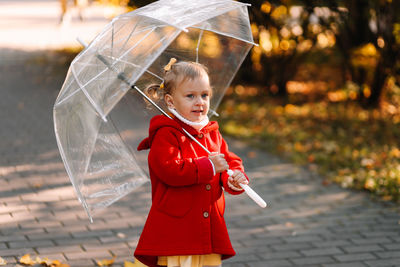 Cute girl holding umbrella while standing outdoors