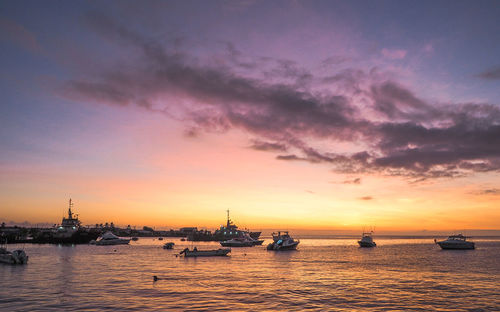 Sailboats moored in sea at sunset