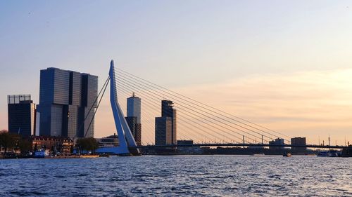 Bridge over river by buildings against sky during sunset