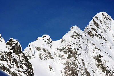 Low angle view of snowcapped mountains against clear blue sky