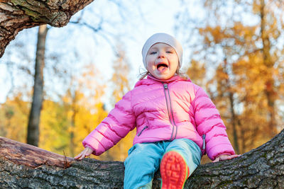 Low angle view of cute boy sitting on tree trunk