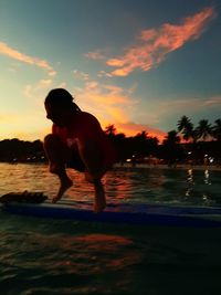 Silhouette boy in sea against sky during sunset