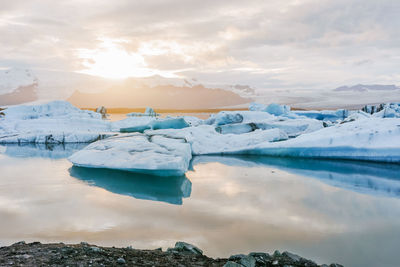 Icebergs melting in calm lake against cloudy sky