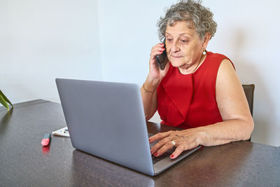 Mid adult woman using phone while sitting on table at home