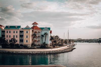 Sailboats in river by buildings against sky