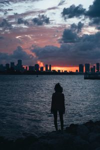 Rear view of silhouette man standing by sea against sky during sunset