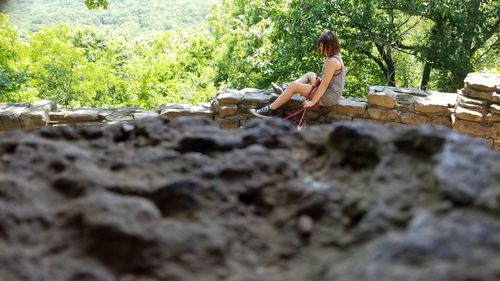 Woman sitting by tree against plants