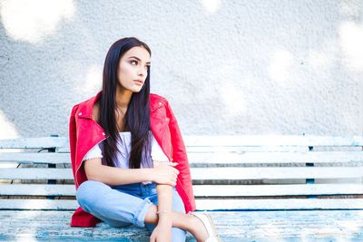 Beautiful young woman sitting on bench against wall