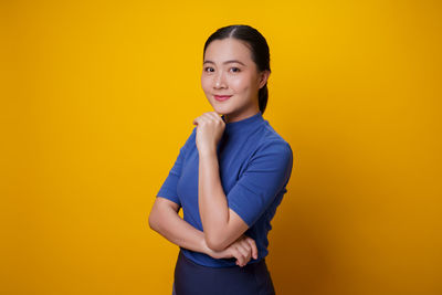 Portrait of smiling young woman against yellow background