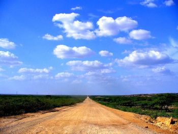 Road passing through field against cloudy sky