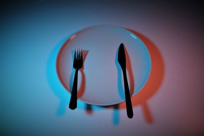 Directly above shot of white dish folk anf knife on plate against blue wall