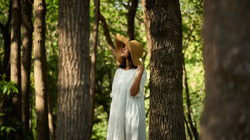 Side view of woman standing by tree trunk in forest