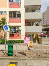 Full length of young woman sitting against building on railing