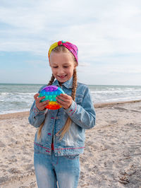 Happy child rainbow pop it toy beach girl walking on sea background antistress sensory simple dimple