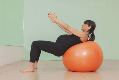 Full length of woman with arms raised on floor against wall