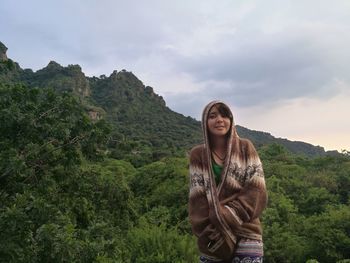 Portrait of smiling young woman standing on mountain against sky
