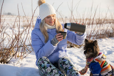 Portrait of young woman using mobile phone while sitting on snow