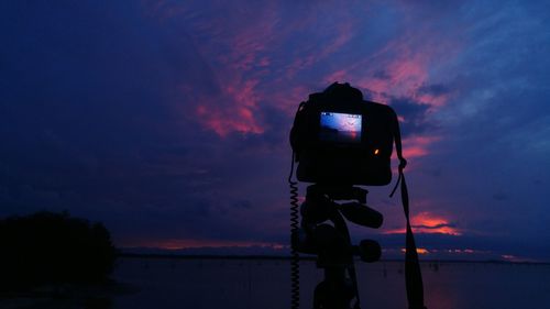 Camera photographing lake against cloudy sky at dusk