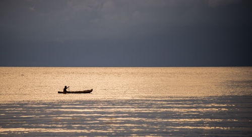 Person sailing boat on sea against sky during sunset