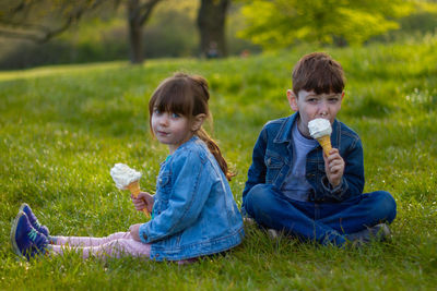 Two children sitting on grass eating ice cream