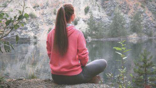 Rear view of woman relaxing on rock by lake