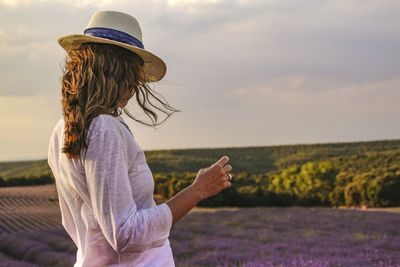 Side view of woman standing on field against sky during sunset