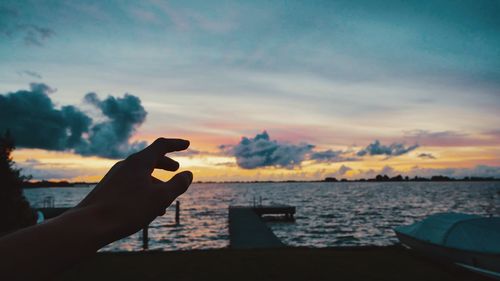 Cropped hand of person reaching sky during sunset