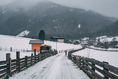 Snow covered road by houses and mountain during winter