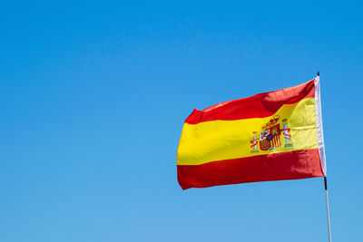 A spanish flag blowing in the wind with blue skies in the background