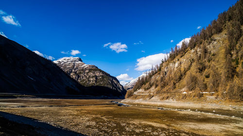 Road by snowcapped mountains against blue sky