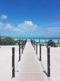 Boardwalk leading towards sea against blue sky