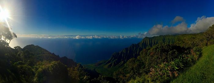Panoramic view of green landscape by sea against blue sky