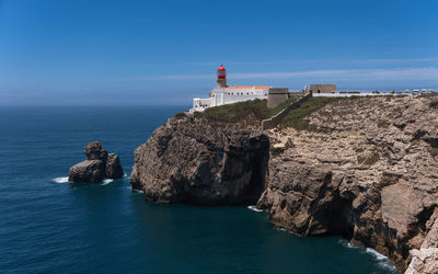 Farol do cabo de são vicente, lighthouse by sea against sky