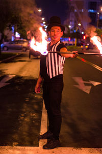 Full length portrait of man performing with fire on street at night