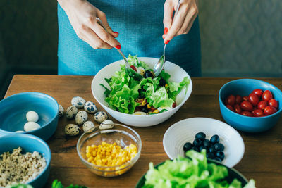 Close-up of a woman mixing green salad in a large bowl.
