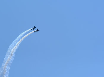 Low angle view of airplanes flying against clear blue sky