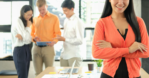 Midsection of smiling businesswoman with colleagues in background