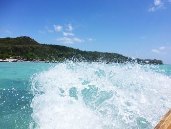 Waves splashing on sea against blue sky