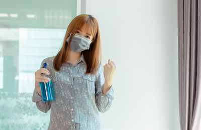 Portrait of a beautiful young woman standing against window