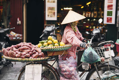 Woman wearing hat selling fruits on bicycle in city