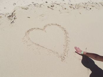 Midsection of person making heart shape on sand at beach