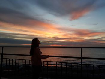 Silhouette woman standing by railing against sea during sunset