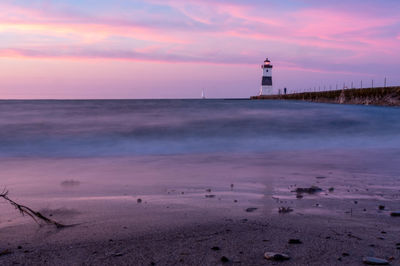 Lighthouse by sea against sky during sunset