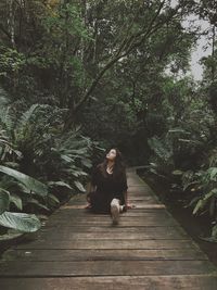 Woman sitting on wooden structure in forest