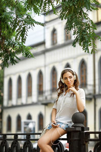 Portrait of young woman sitting against buildings in city