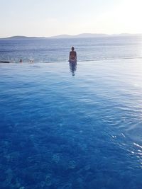 Rear view of woman sitting at infinity pool against clear sky