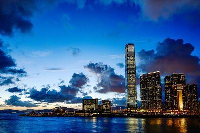 Illuminated city by river against sky