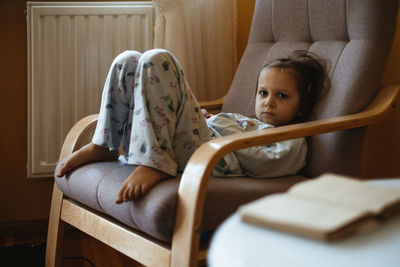 Bored sad toddler child lonely at home sitting on armchair. sad relaxed candid kid at home in cozy