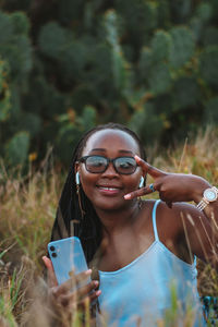 Portrait of young woman wearing sunglasses while standing against trees