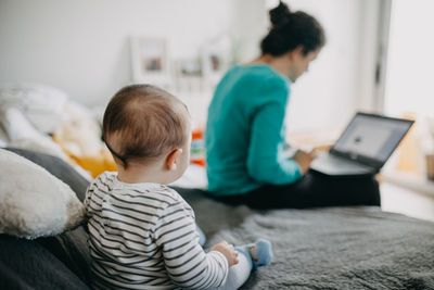 Rear view of baby  watching mother working from home